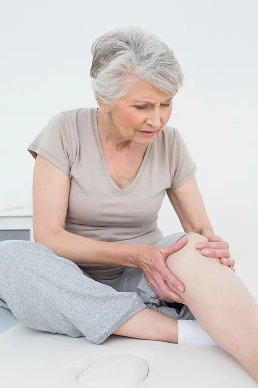 Older adult holding her knee in pain, representing chronic knee discomfort